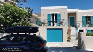A two-story building with blue shutters, a staircase, and a car parked in front.