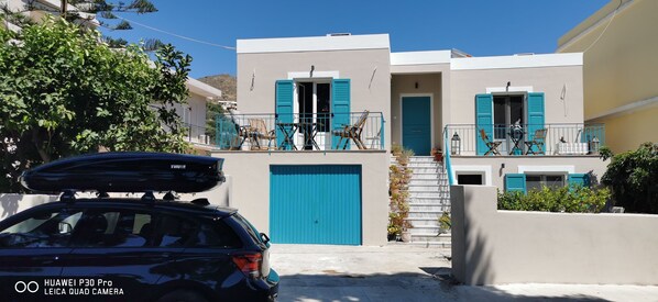 Un immeuble de deux étages avec des volets bleus, un escalier et une voiture garée devant.