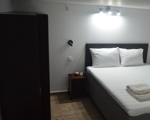 A bedroom with a bed, a nightstand, a wardrobe, and a wall-mounted light fixture.