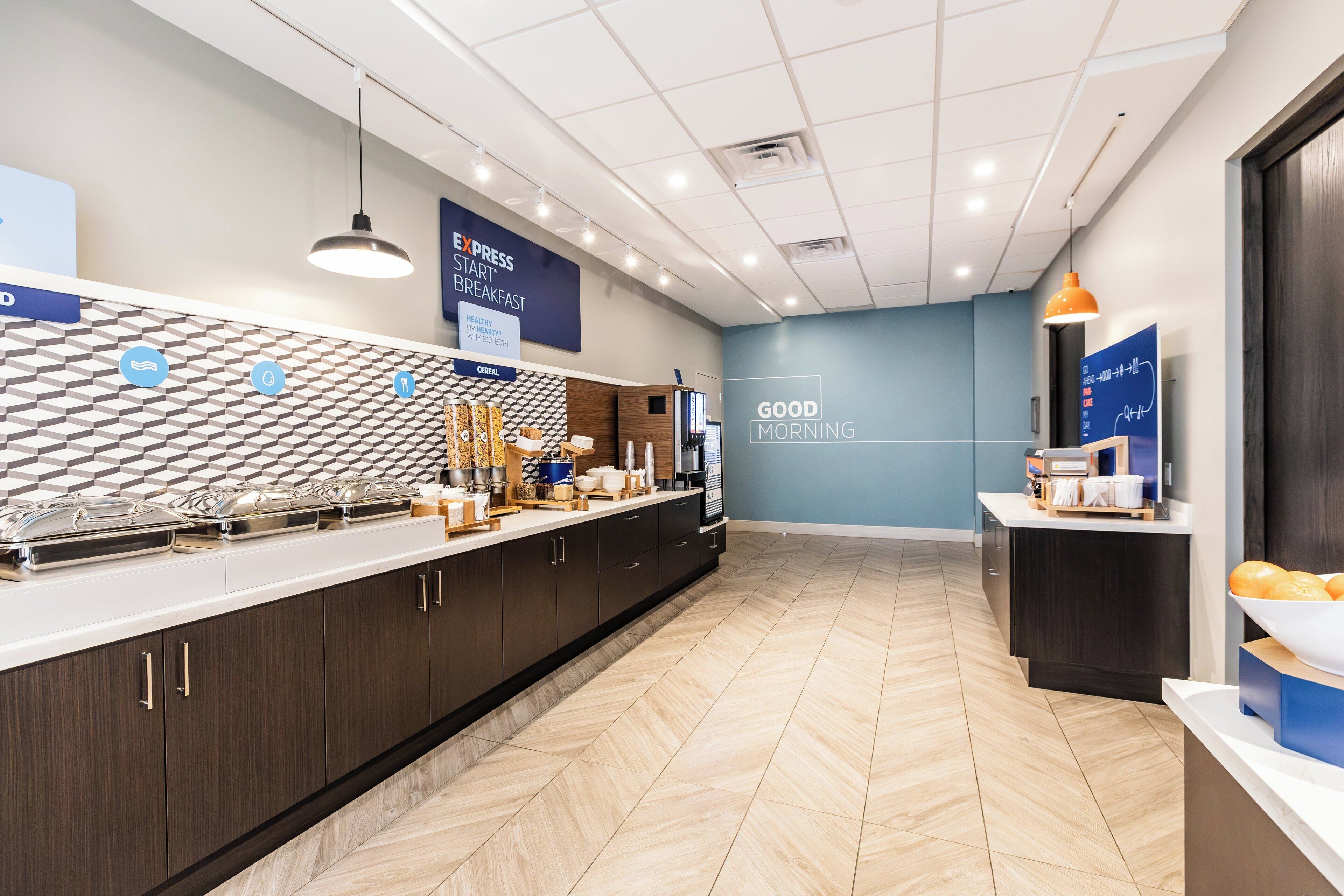 A modern kitchen area with a long counter, various appliances, and a patterned wall.