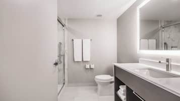 Un baño moderno con cabina de ducha de vidrio, inodoro blanco y tocador con un espejo grande.