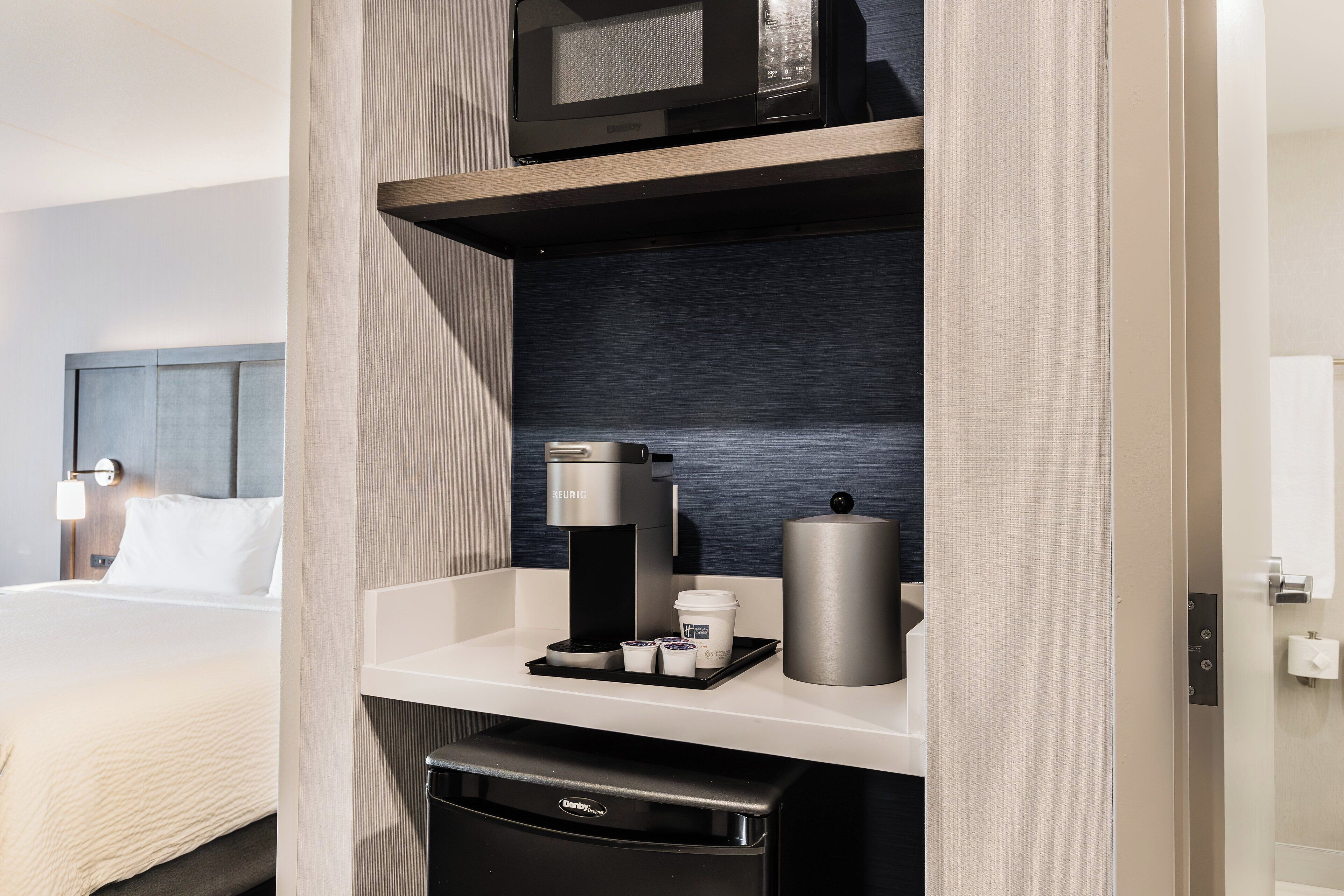 A hotel room with a bed, a coffee machine, a microwave, and a small refrigerator.