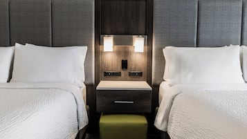 Una habitación de hotel con dos camas, una mesita de noche con lámpara y un reposapiés verde.