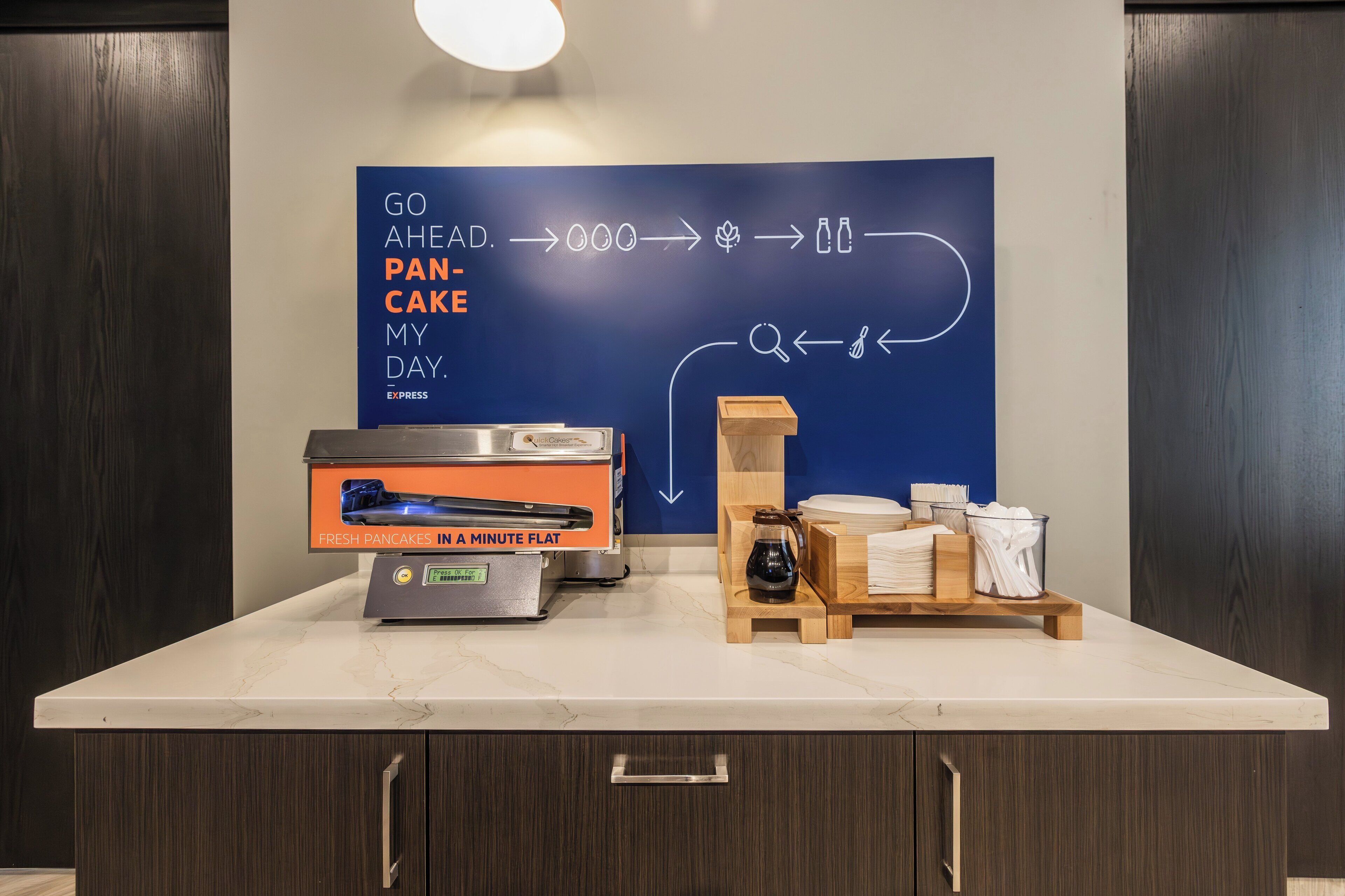 Una encimera de cocina con una cafetera, un cartel que explica cómo hacer panqueques y una estación de café con tazas y un hervidor.