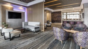 A modern lobby with a grey sofa, patterned armchairs, a flat-screen TV, and a bar area with seating. - Holiday Inn Express & Suites Toronto Airport South by IHG (Toronto)