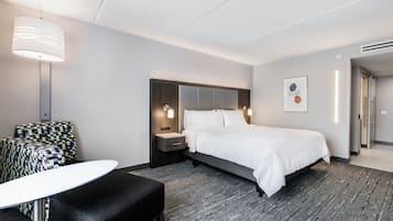 A modern hotel room with a large bed, a desk, a patterned armchair, and a small table.