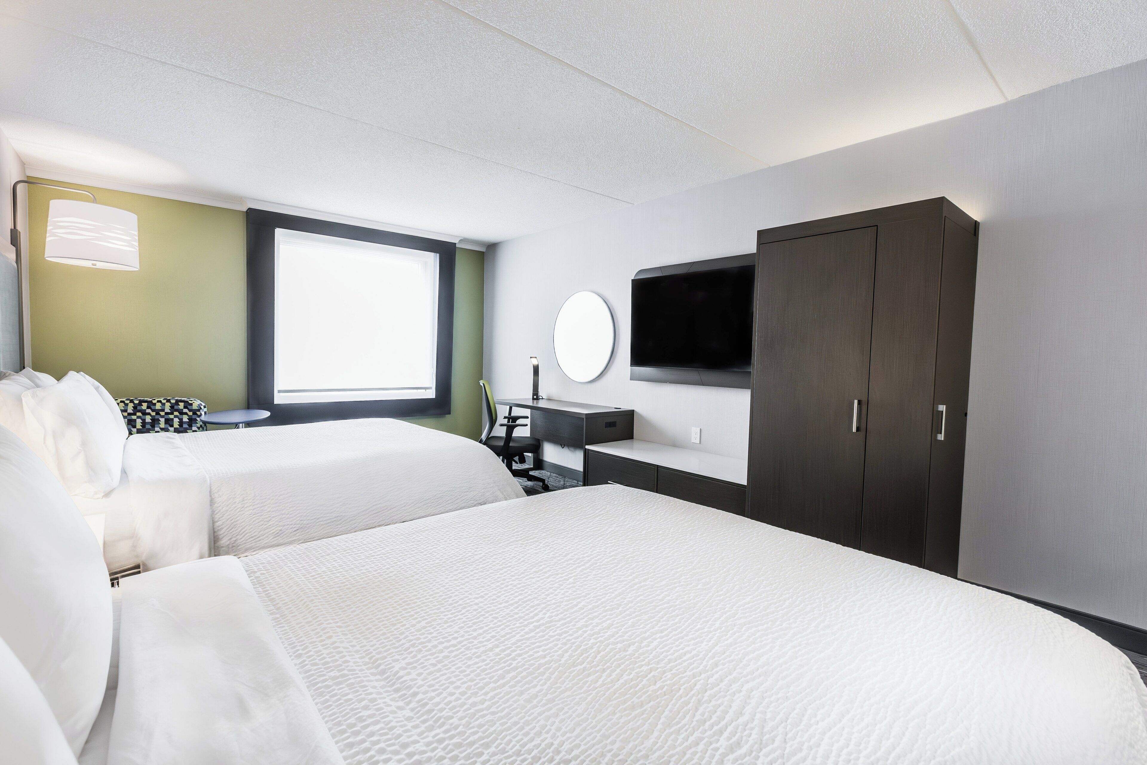 A hotel room with two beds, a desk, a chair, a TV, and a wardrobe.