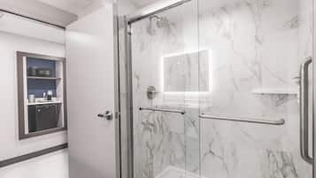 A modern bathroom with a glass shower enclosure, marble walls, and a built-in microwave shelf.