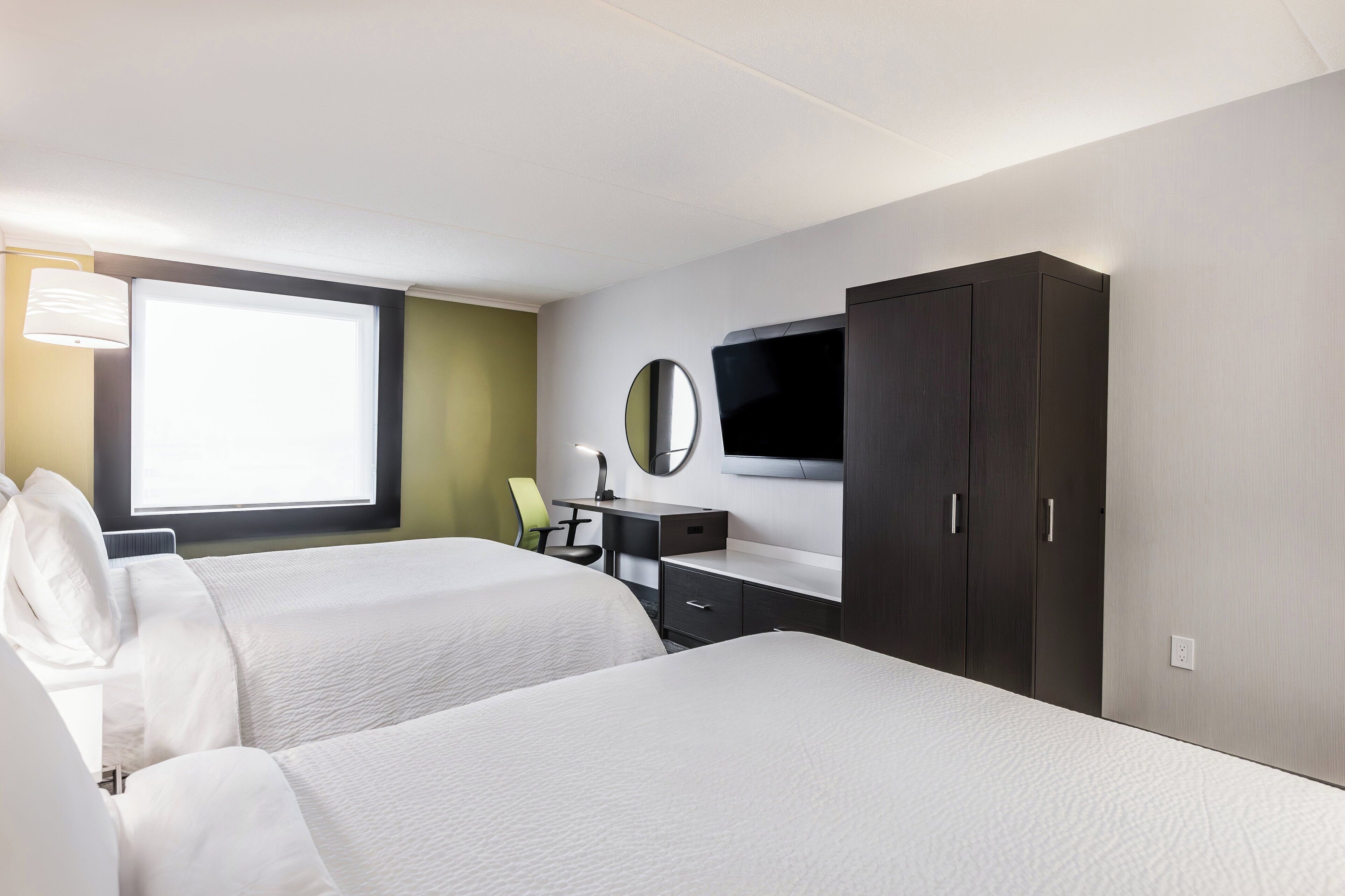 Une chambre d’hôtel avec deux lits, un bureau, une chaise, une télévision et une armoire.