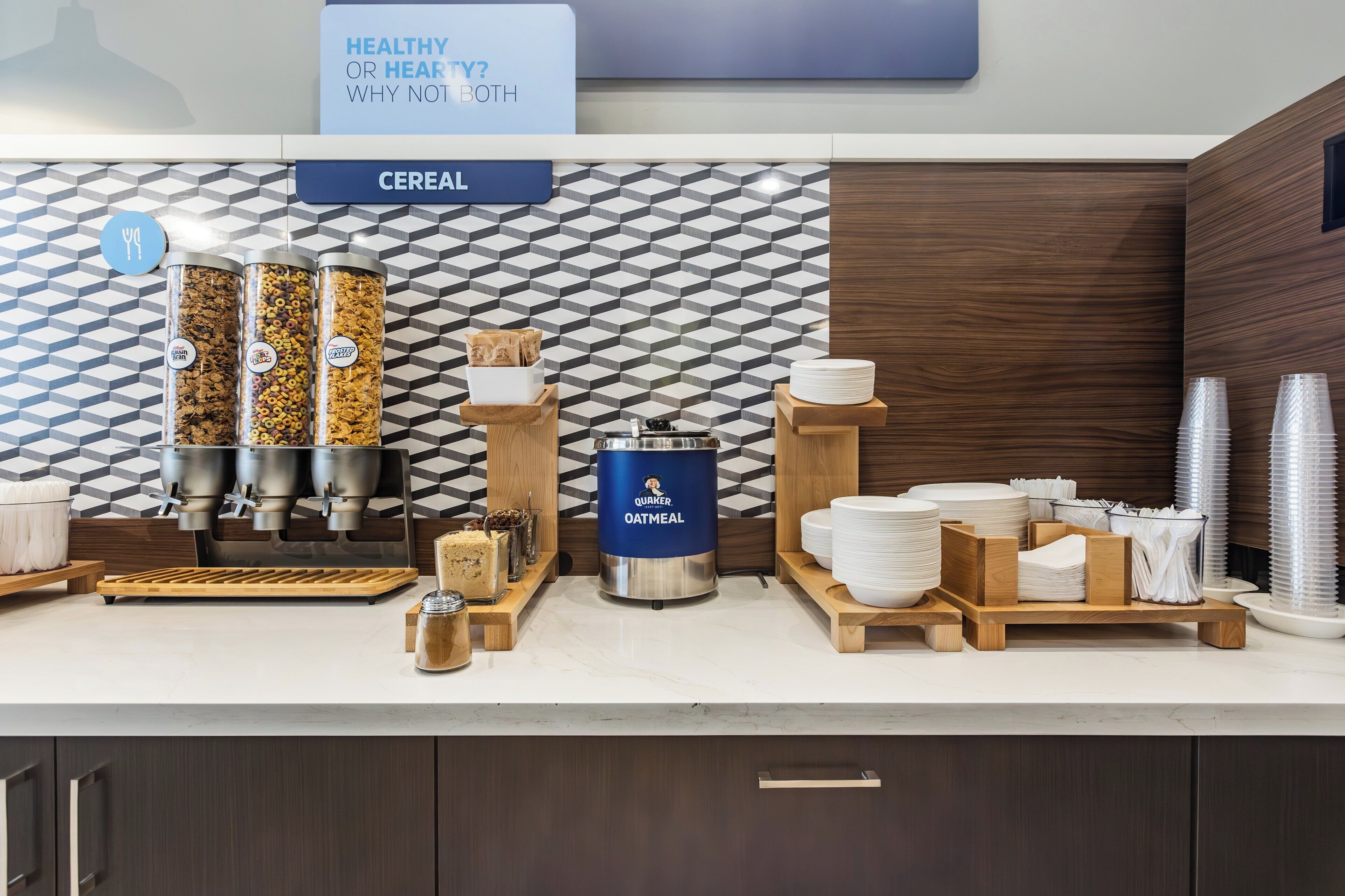 A breakfast bar with cereal dispensers, an oatmeal dispenser, and a sign asking "Healthy or Healty? Why not both".