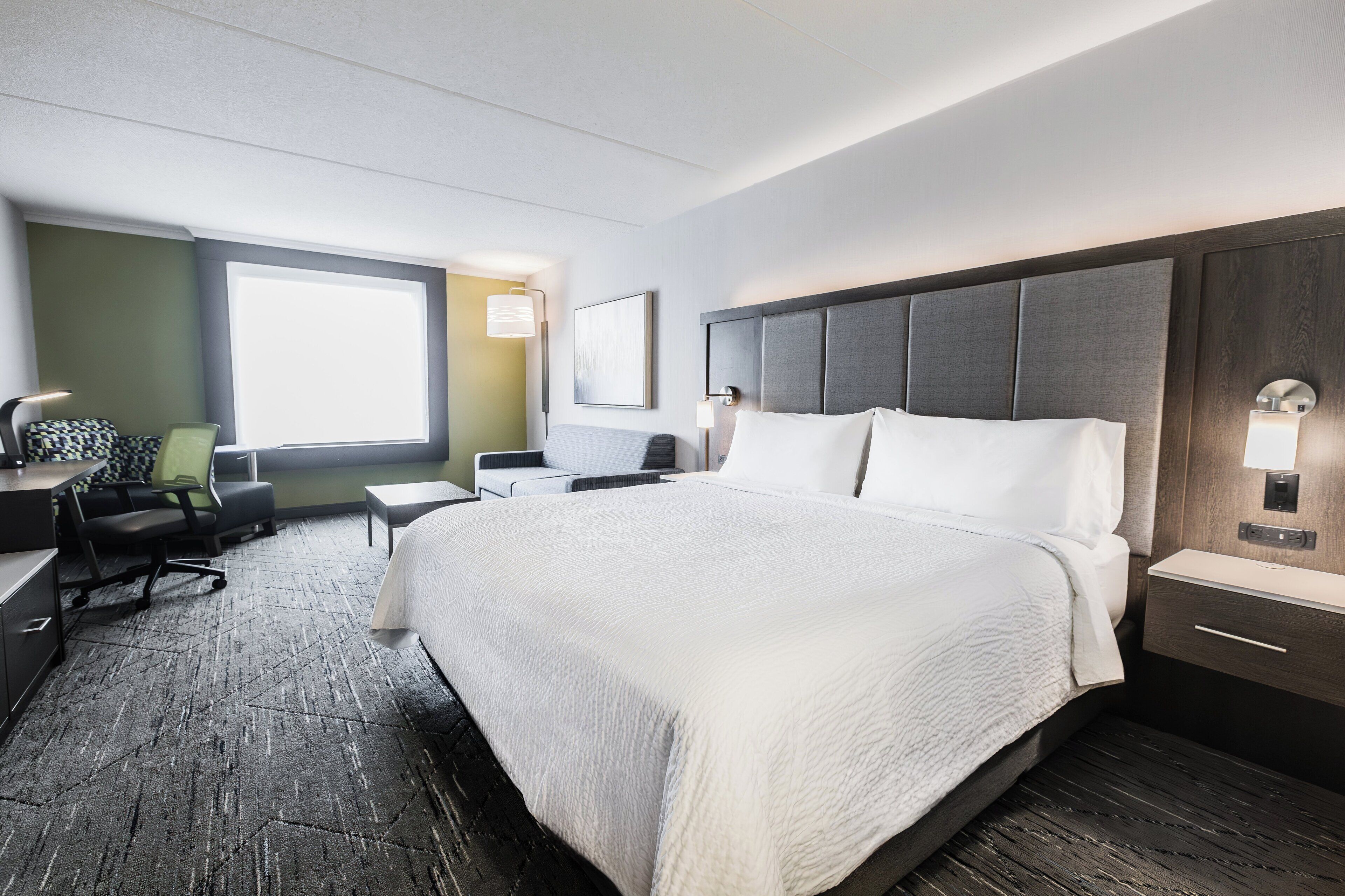 A hotel room with a large bed, a desk, a chair, and a window.