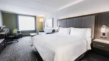 A hotel room with a large bed, a desk, a chair, and a window.