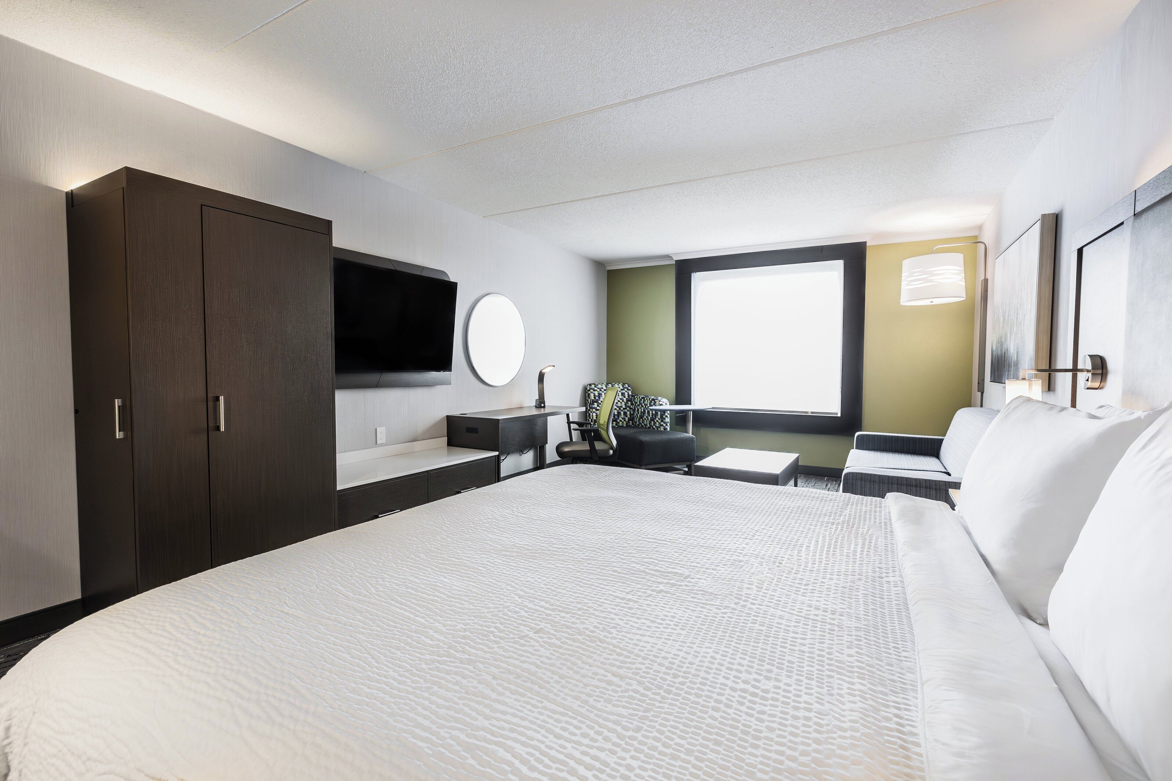 Una habitación de hotel con una cama grande, un escritorio, una silla, un televisor y una ventana.