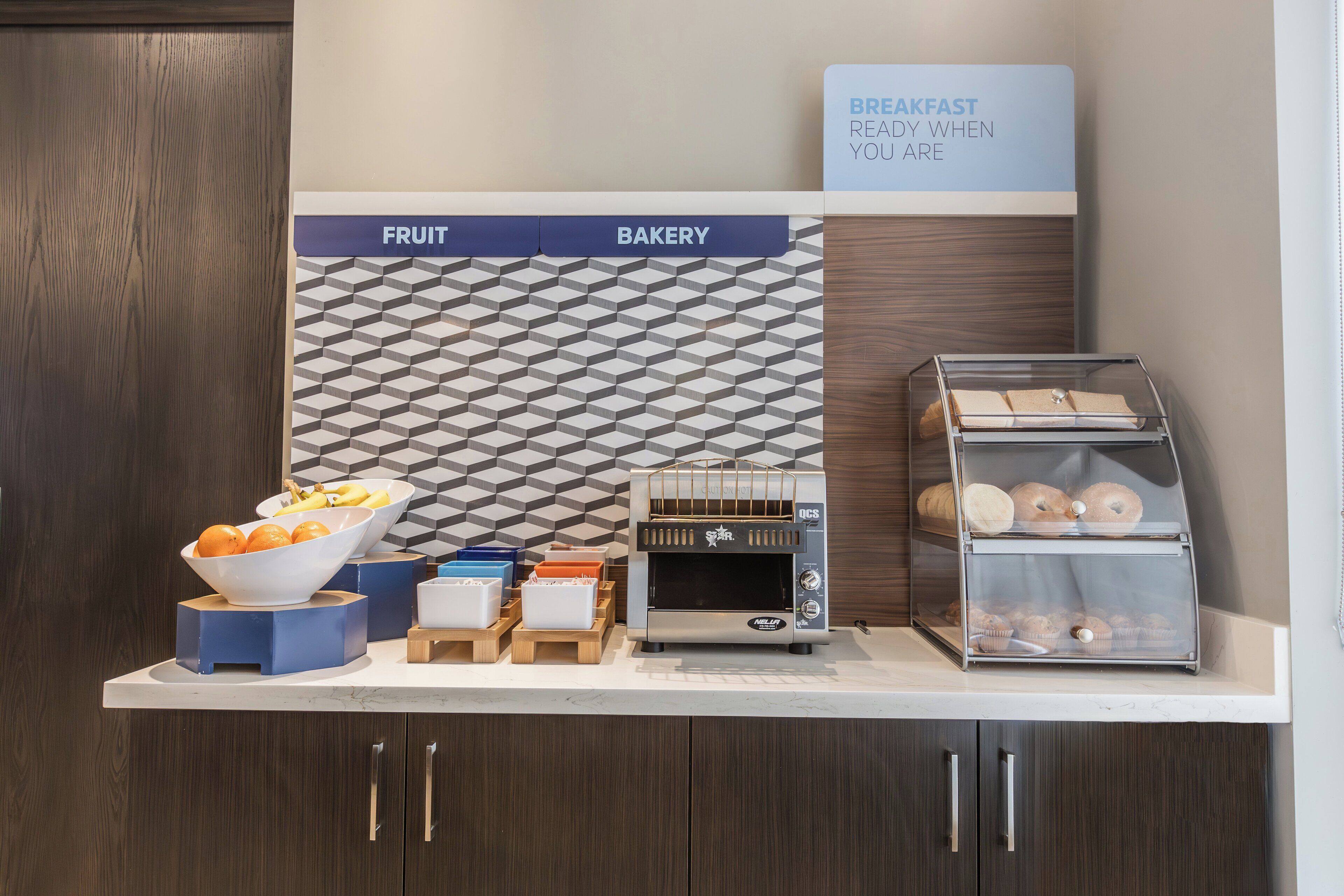 A breakfast station with a fruit bowl, bakery display, and a food display case.
