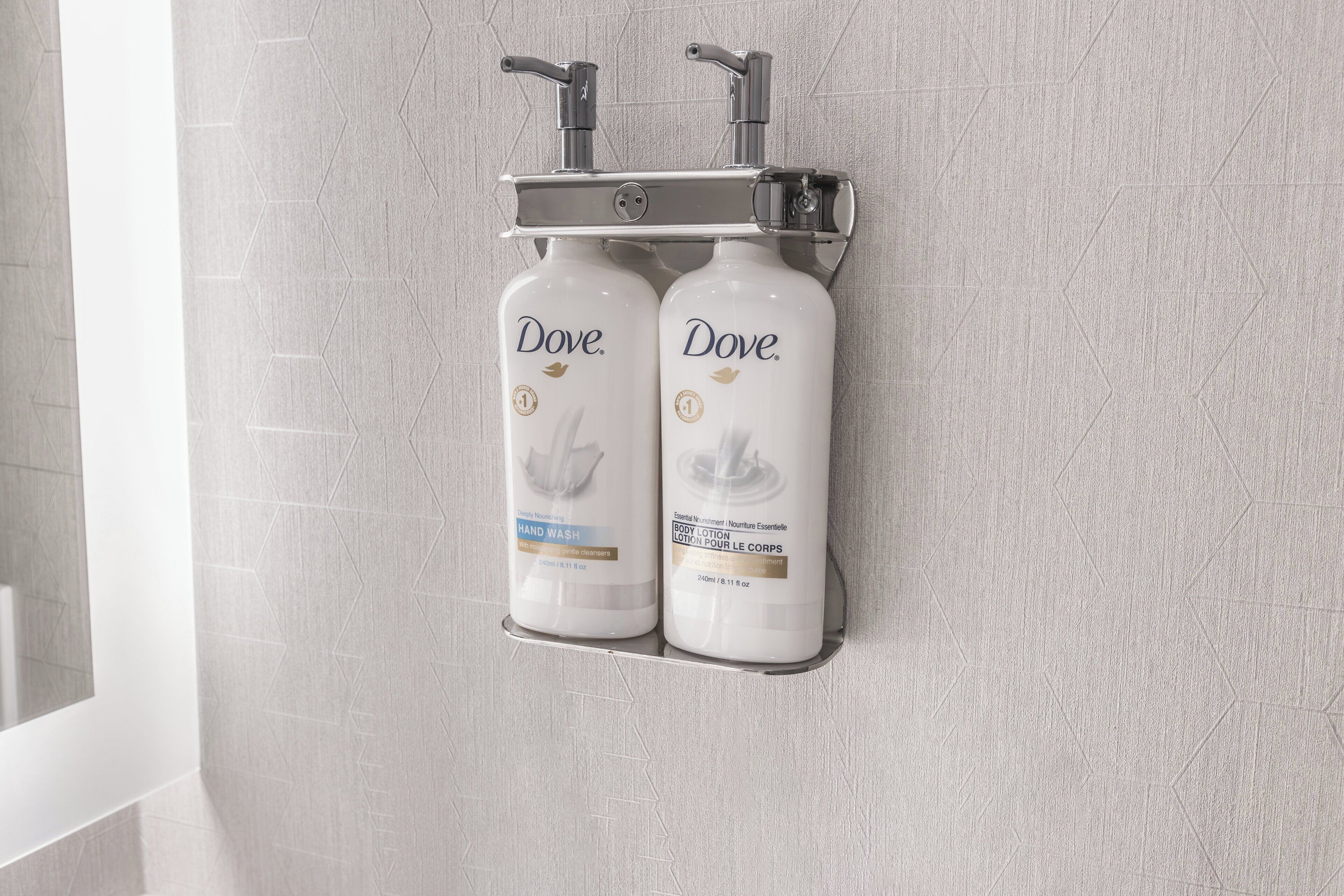 A bathroom with two Dove hand wash bottles mounted on a wall-mounted holder.