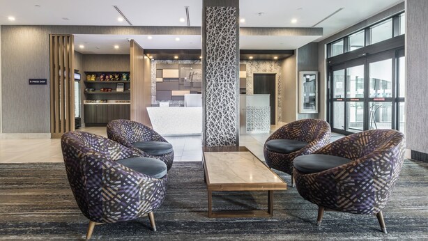 A lobby with patterned armchairs, a central coffee table, and a reception area with a sign reading "E-Press Shop". - Holiday Inn Express & Suites Toronto Airport South by IHG (Toronto)