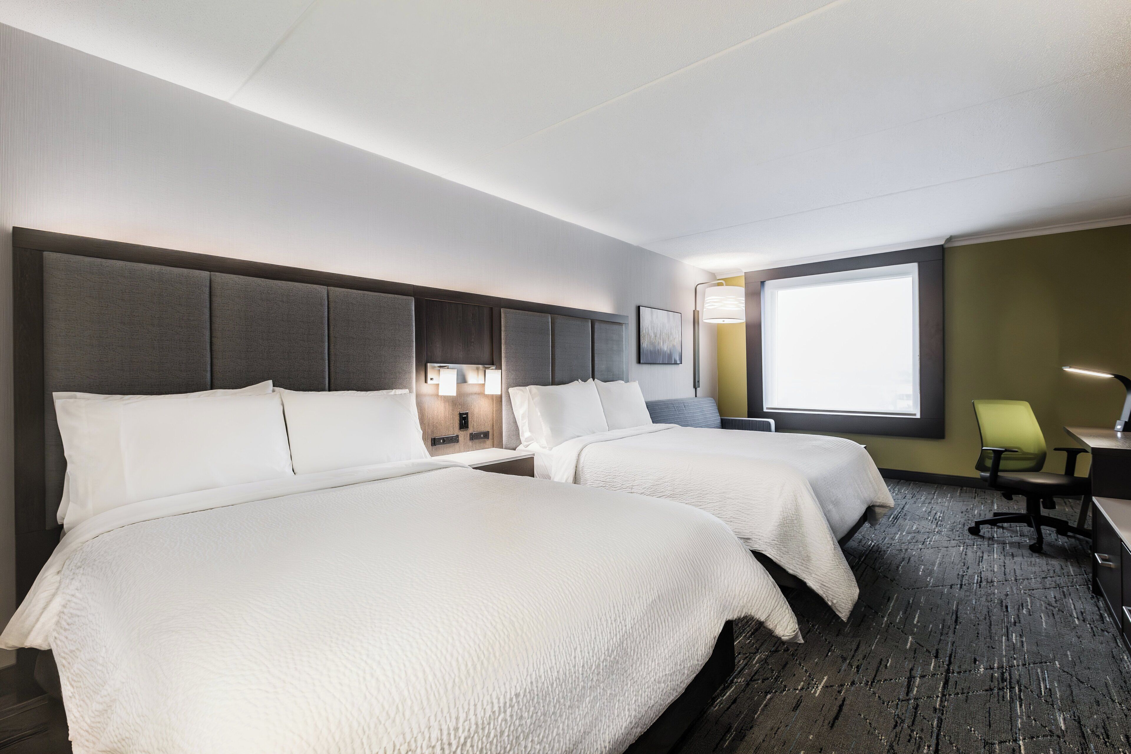 Une chambre d’hôtel avec deux lits, un bureau, une chaise et une grande fenêtre.