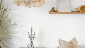 A cozy living room with a hanging light fixture, a small wooden side table with a decorative item, a potted plant, and a white sofa with a cushion. - 4 bedroom private home in Coronado Historic District by PHX Stays (Phoenix)