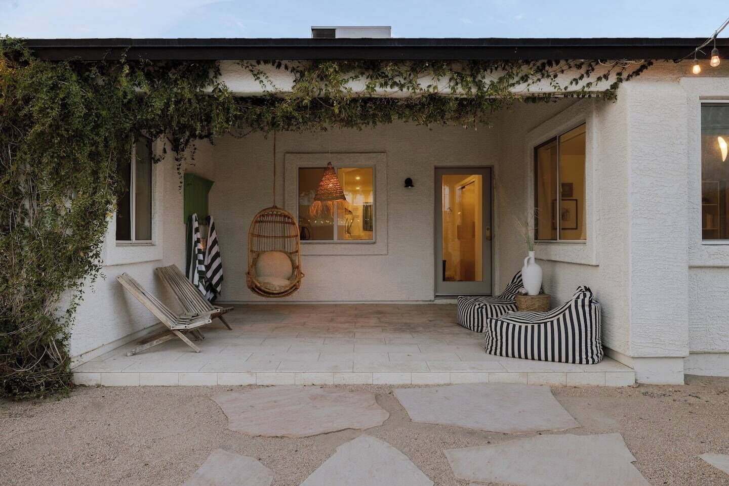 A covered patio with a swing chair, cushioned seating, and a hanging light fixture.