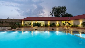 A swimming pool with lounge chairs and a building with a red roof. - Paandora Grand Udaipur (Udaipur)