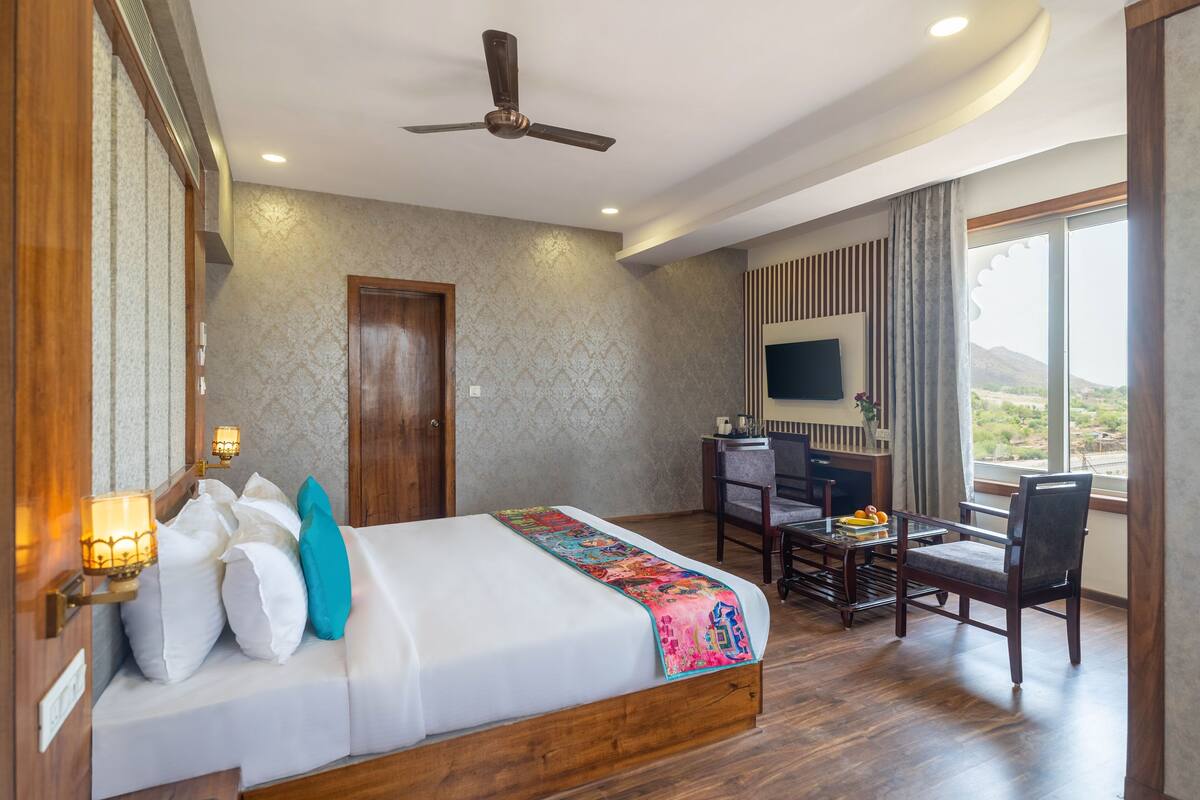 A hotel room with a bed, desk, chair, TV, and a view of the outdoors.