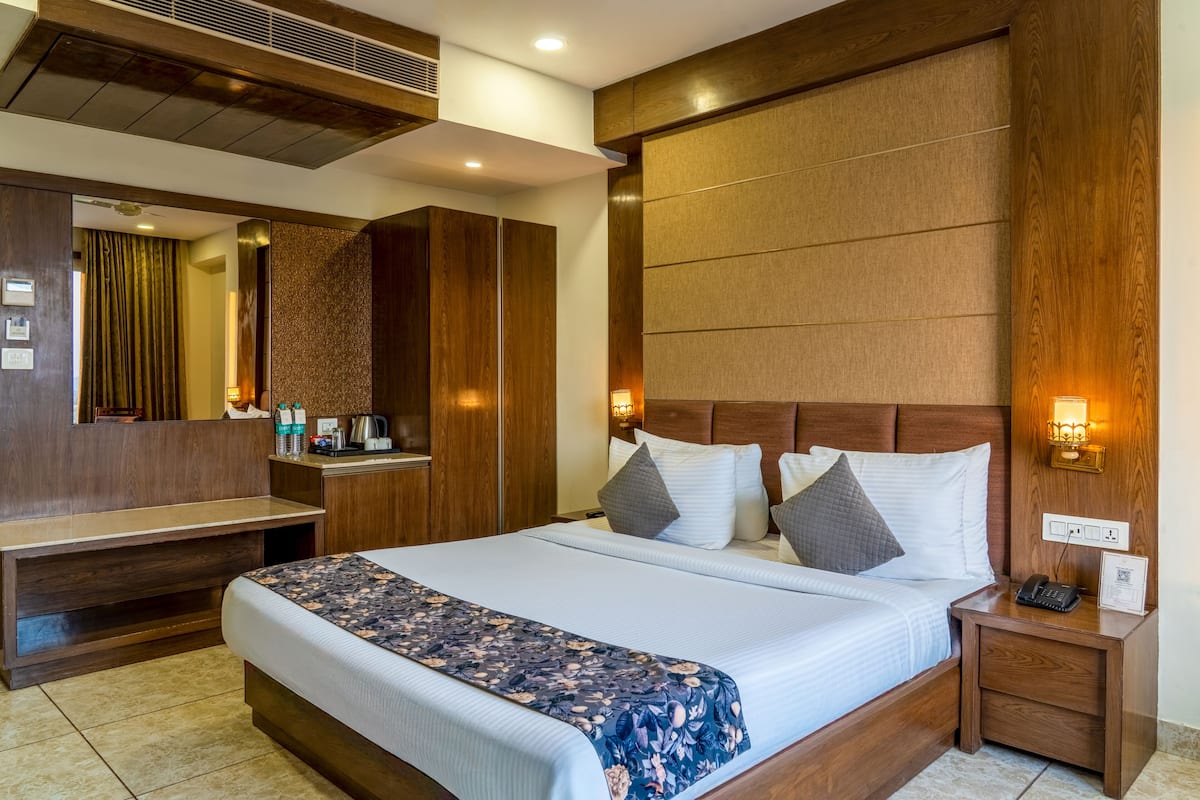 A hotel room with a large bed, wooden headboard, bedside table with a phone and lamp, and a mirror.