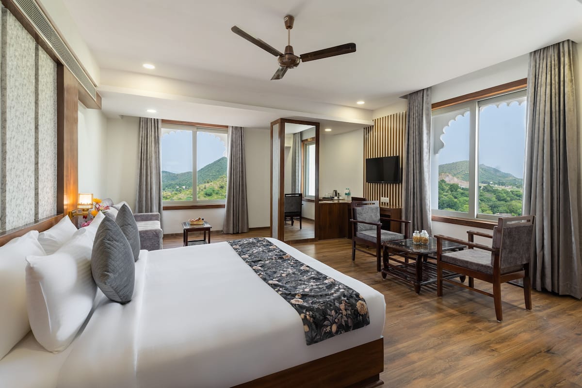 A hotel room with a large bed, a desk, a chair, a television, and a view of the outdoors.