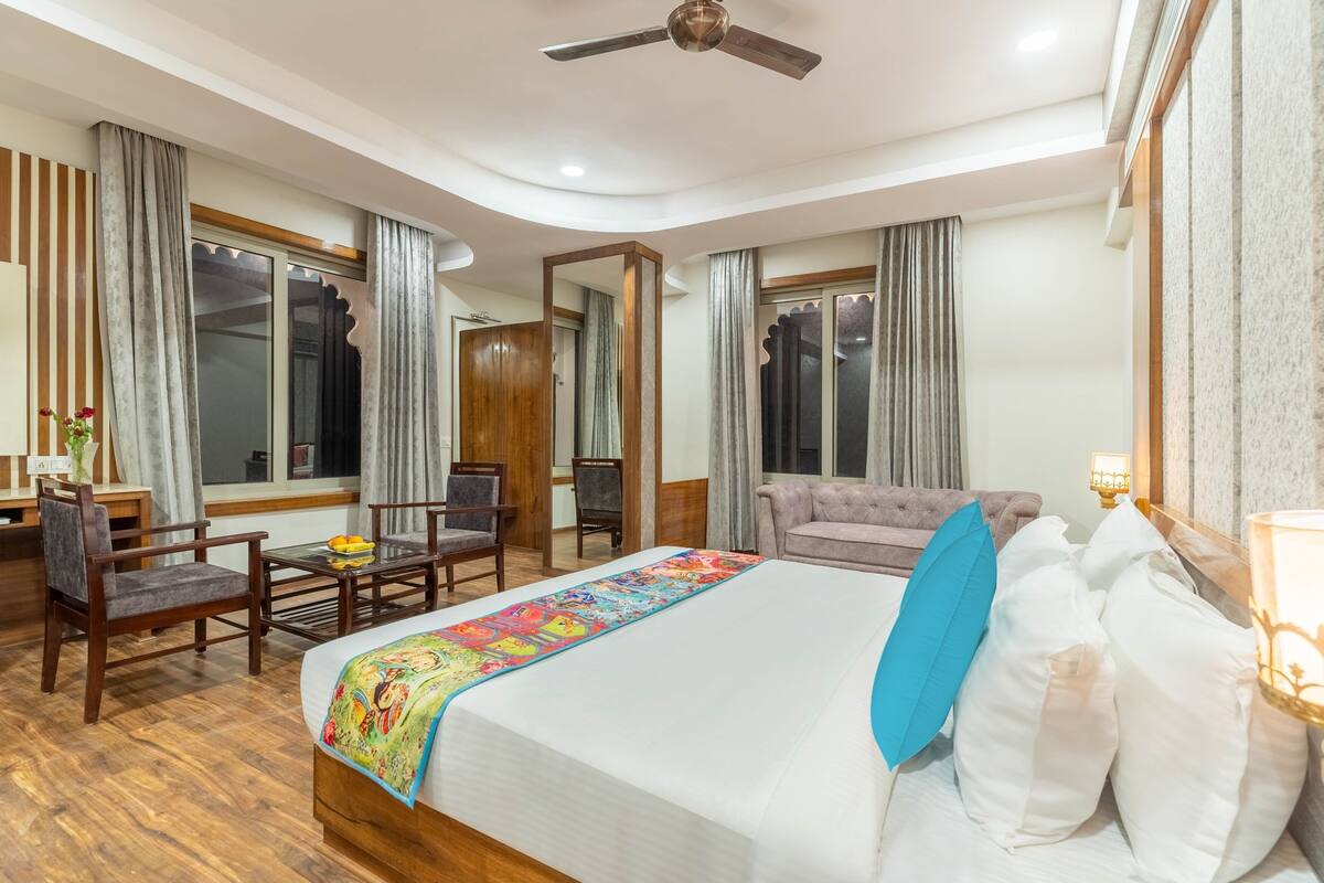 A hotel room with a bed, a desk, a chair, a sofa, and a ceiling fan.