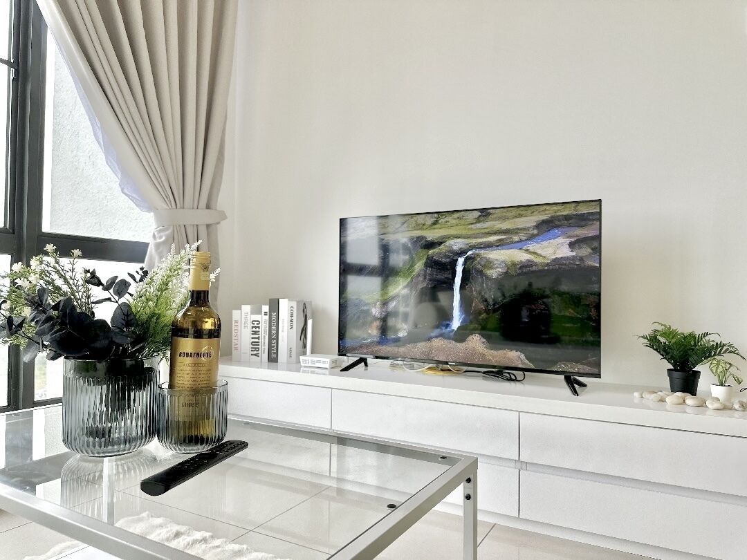 A modern living room with a flat-screen TV mounted on the wall, a glass coffee table, and a remote control on it.