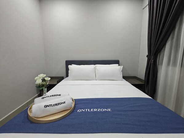 A neatly made bed with white linens and a blue blanket, a wooden tray with towels, and a vase with white flowers on a nightstand.