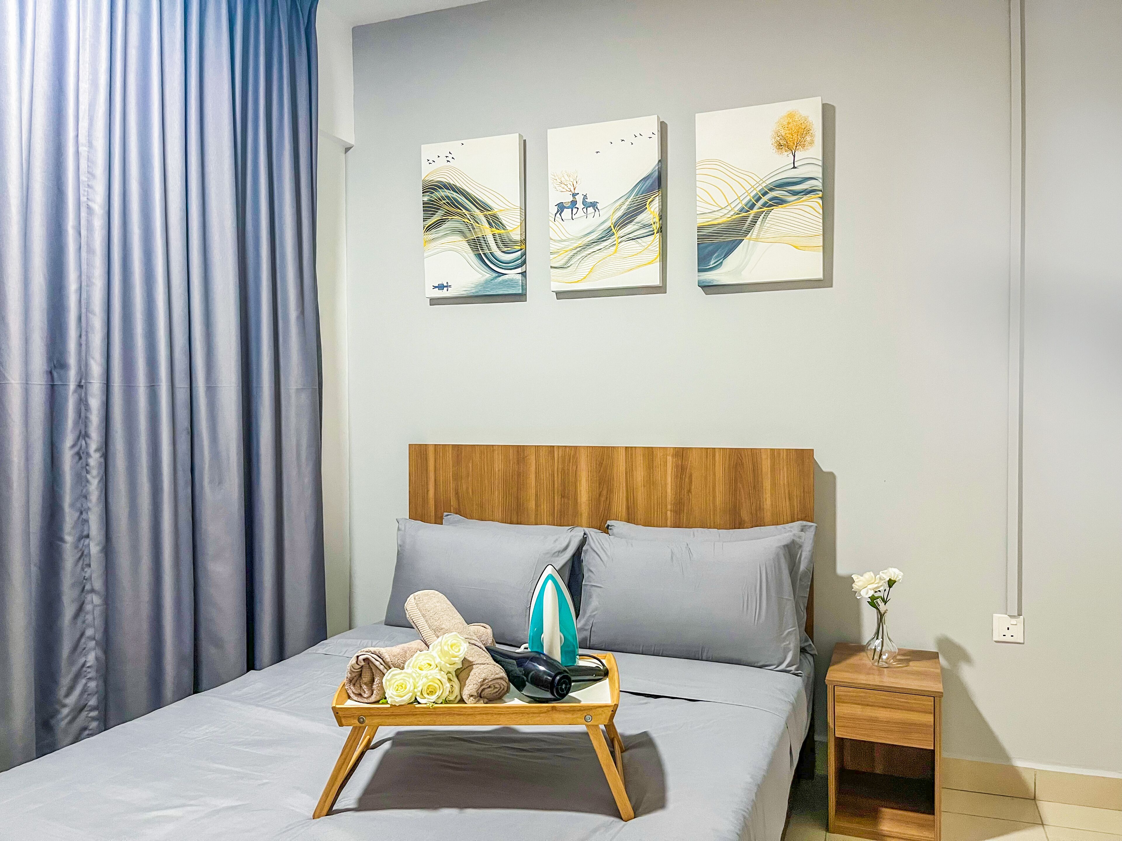 A neatly made bed with a wooden headboard, a bedside table with a vase of flowers, and three abstract paintings on the wall.