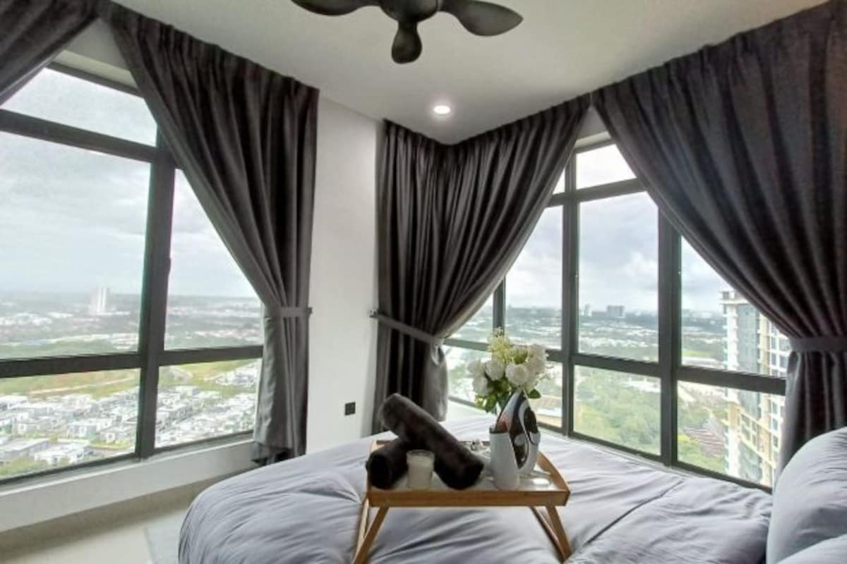 A hotel room with a large window, a bed, a bedside table with a vase of flowers, and a ceiling fan.