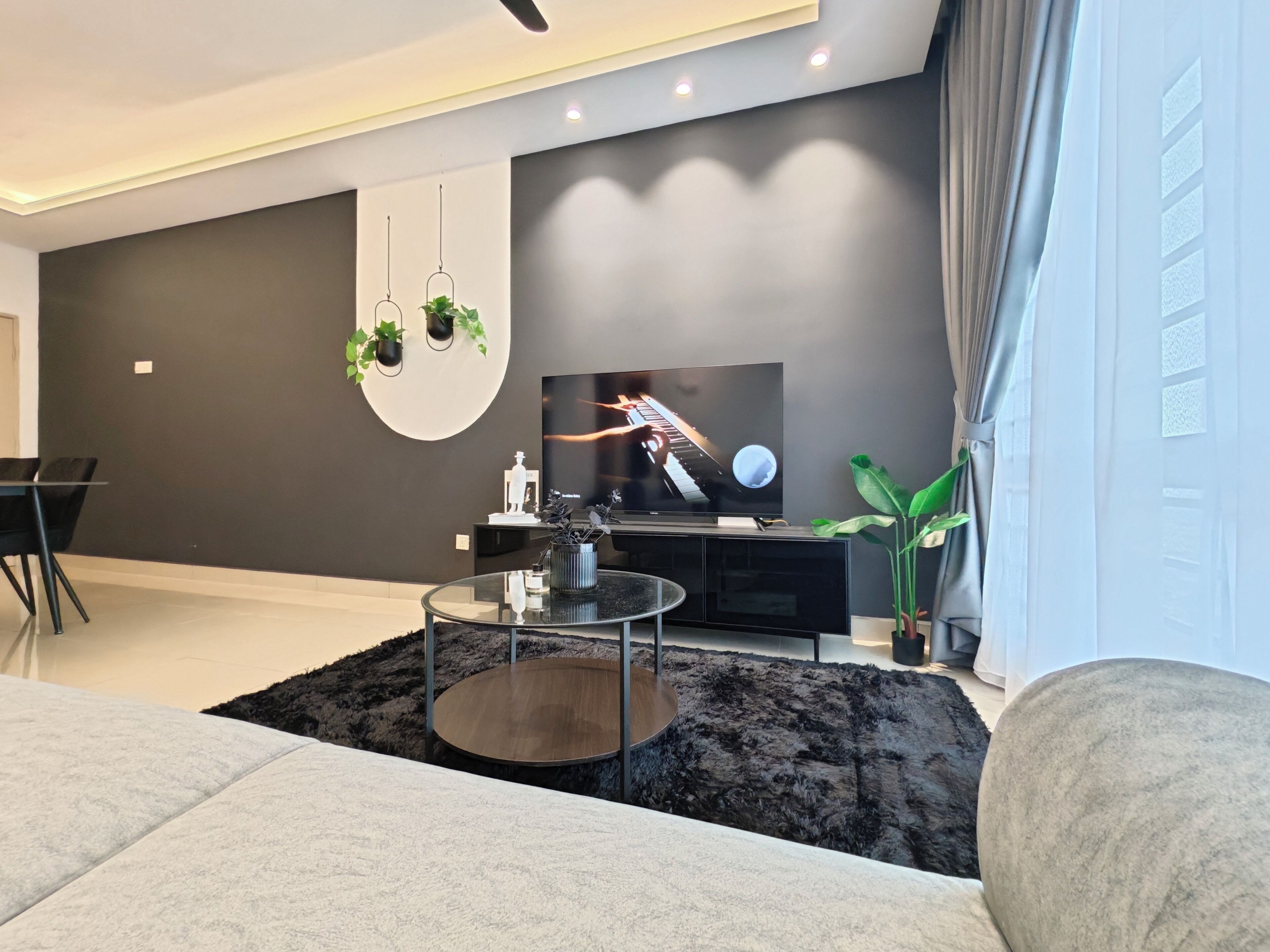 A modern living room with a flat-screen TV, a glass coffee table, and a dark rug.