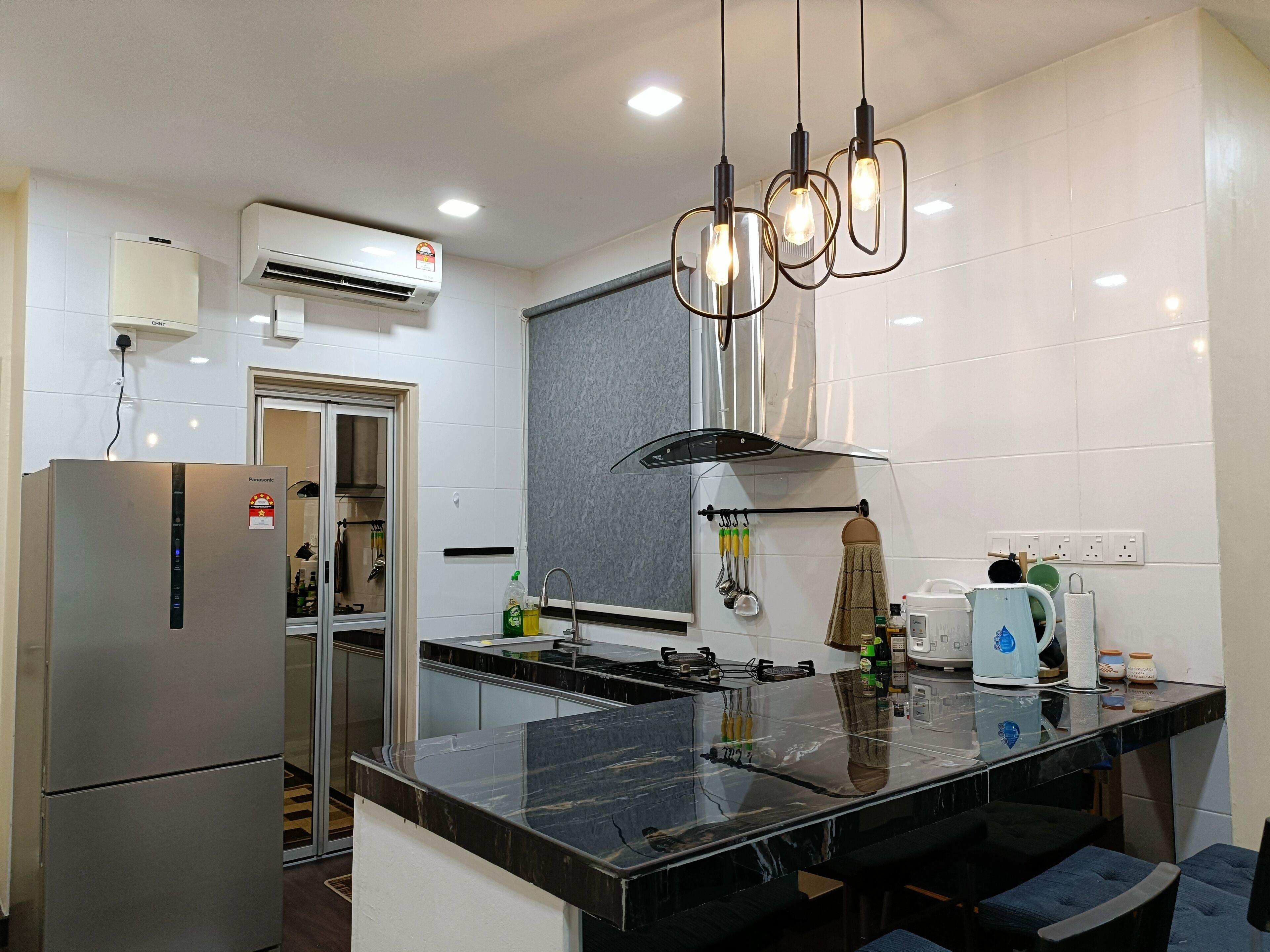 A modern kitchen with a stainless steel refrigerator, a built-in oven, a gas stove, and a black marble countertop.