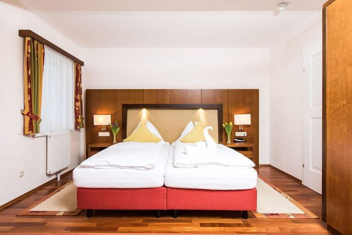 Una cama doble con colcha roja de lunares, dos lámparas de noche, un cabecero de madera y un radiador en la pared.