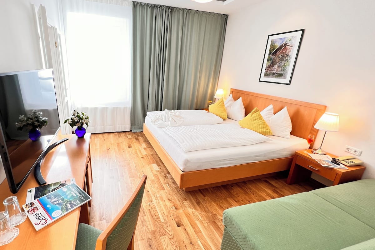 Une chambre d’hôtel équipée d’un lit, d’une table de chevet, d’une lampe, d’une télévision et d’une fenêtre avec des rideaux.