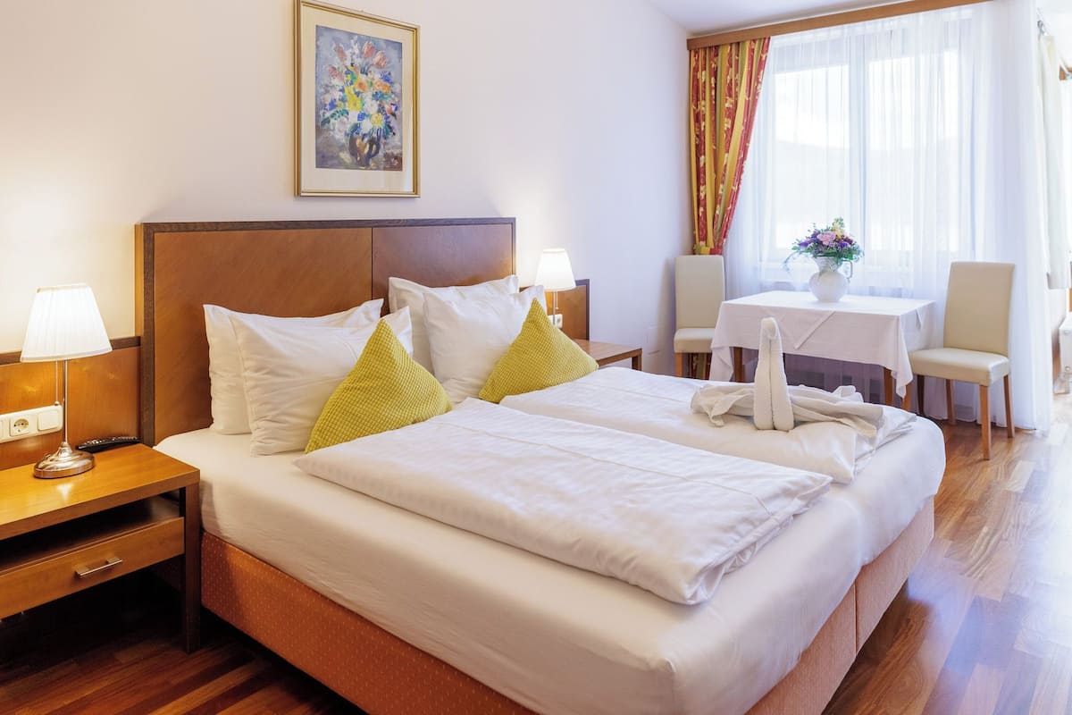 Una habitación de hotel con una cama grande, mesitas de noche con lámparas, una pequeña mesa con un florero y una silla.