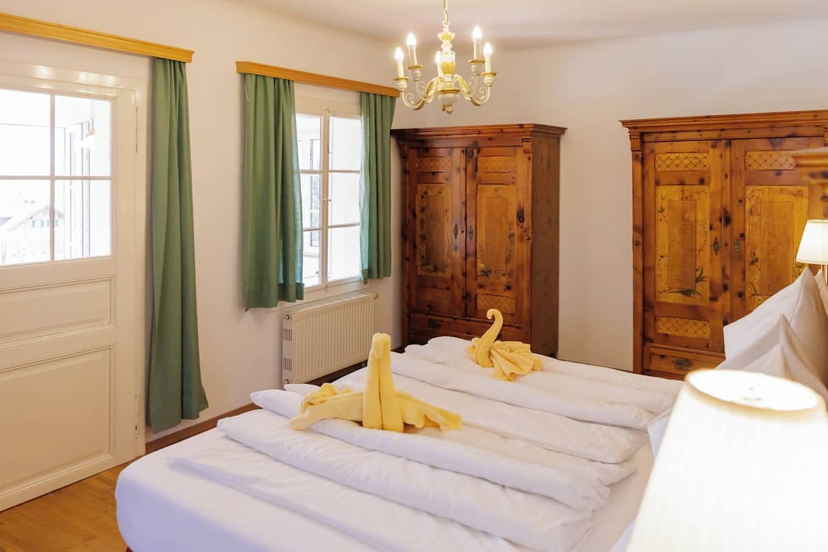 Habitación de hotel con una cama grande, armario de madera y una ventana con cortinas.