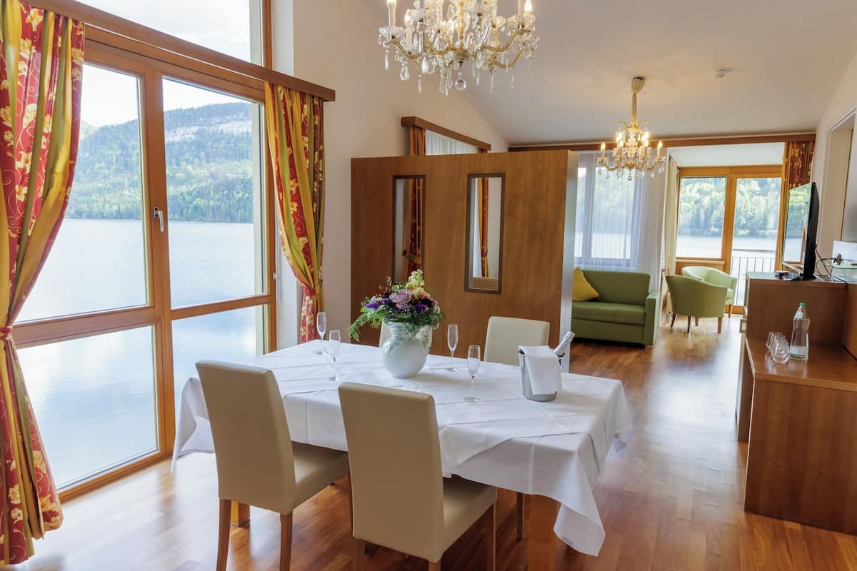 Un comedor con una mesa preparada para cuatro personas, un jarrón de flores y vistas a un lago.