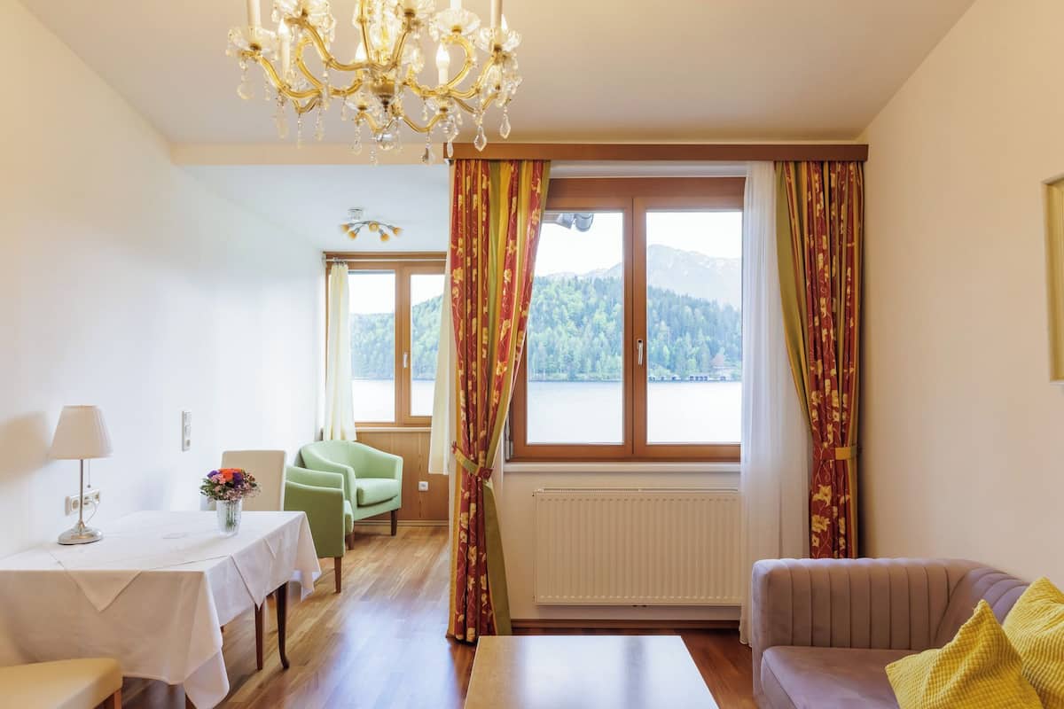 Una habitación con una mesa de comedor, un sofá, una silla, una araña y una ventana con cortinas.