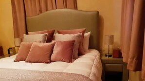 Cama bem arrumada com colcha estampada e vários travesseiros em tons de rosa e bege.