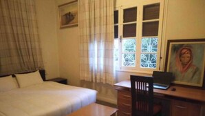 Quarto com cama, escrivaninha, cadeira e janela com detalhes em ferro.