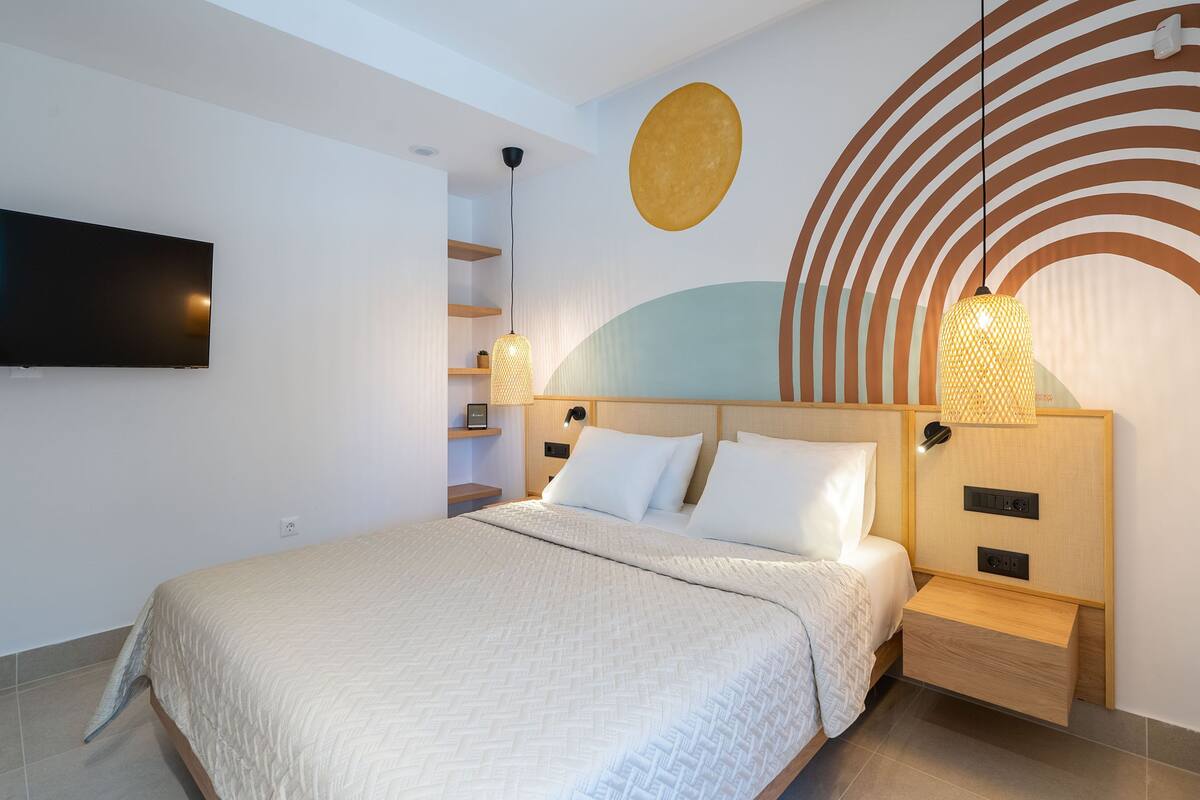A modern hotel room with a large bed, a flat-screen TV mounted on the wall, and a unique wall design with circular patterns.