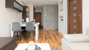 Una sala de estar moderna con un sofá blanco, una zona de comedor con una mesa y sillas blancas, y piso de madera.
