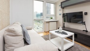 Un salón moderno con un sofá, una mesa de centro, un televisor montado en la pared y un balcón con vistas a la ciudad.