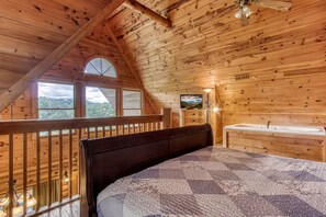 Une chambre de style cabane en bois, avec un grand lit, une commode en bois, une fenêtre donnant sur les montagnes et un ventilateur de plafond.