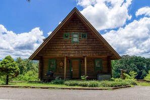 Une cabane en bois avec un toit à deux versants, une véranda à l’avant et une porte surmontée d’une fenêtre.