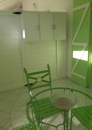 Ein Zimmer mit einem grünen Metallstuhl und -tisch, weißen Schränken und einer grünen Tür.