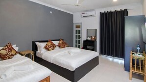 Habitación de hotel con dos camas, un ventilador de techo, un equipo de aire acondicionado, un espejo, un televisor y una mesita con una botella de agua.