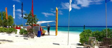 A beach with white sand, clear blue water, and several flags.
